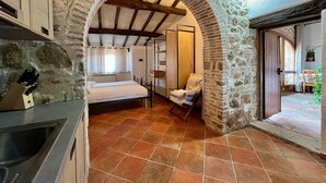 A rustic room with a stone archway, a bed, a wooden chair, and a view of the outside. - Podere Cagnesi: Relaxation in nature (Podere Cagnesi)
