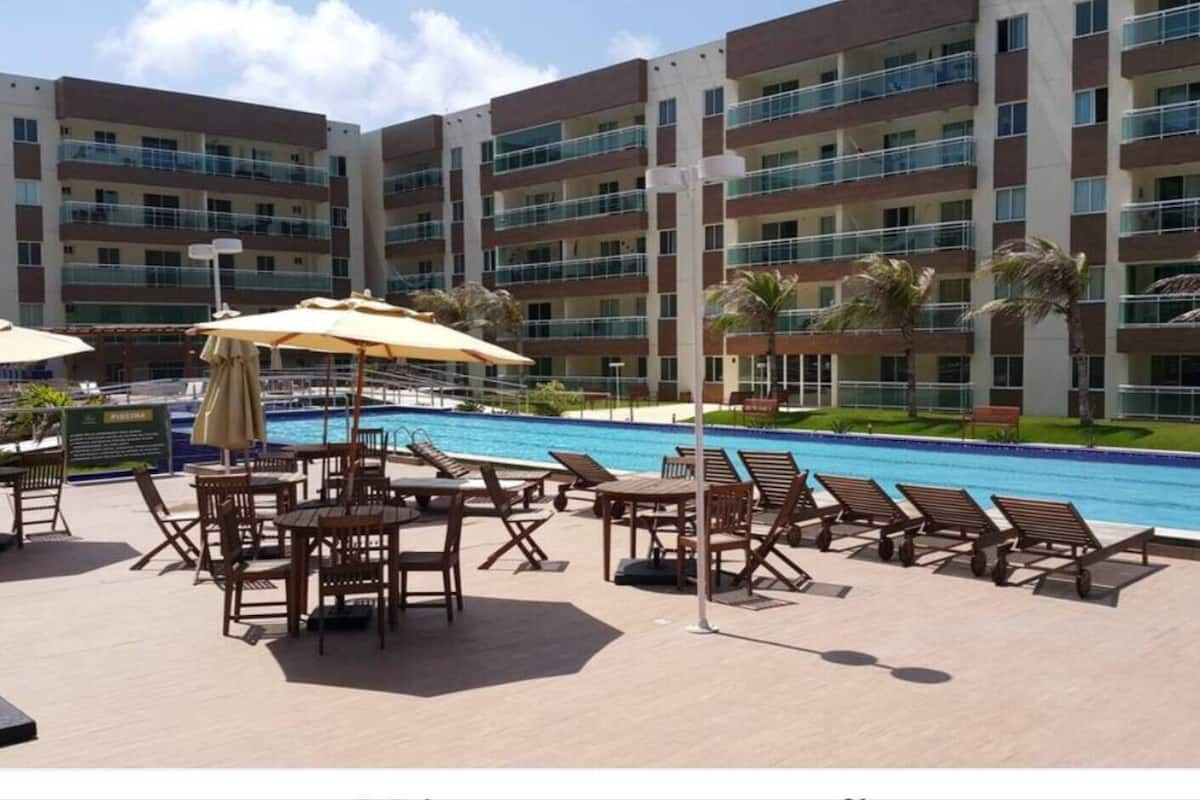 Un espace piscine d’hôtel avec des chaises longues et des tables, entouré d’un immeuble à plusieurs étages doté de balcons.