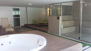 A spa area with a hot tub, green chairs, and a glass-enclosed shower area. - VG Fun Praia do Futuro (Fortaleza)