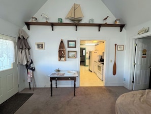 A room with a wooden table, a shelf with decorative items, a door leading to a kitchen, and a hanging wooden bat. - Sanderling - Spacious 4BR home with fenced in back yard & dog friendly. (Chincoteague)