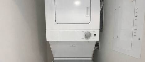 Un lavadero pequeño y blanco con lavadora y secadora integradas, un panel de control y un cuadro eléctrico instalado en la pared.