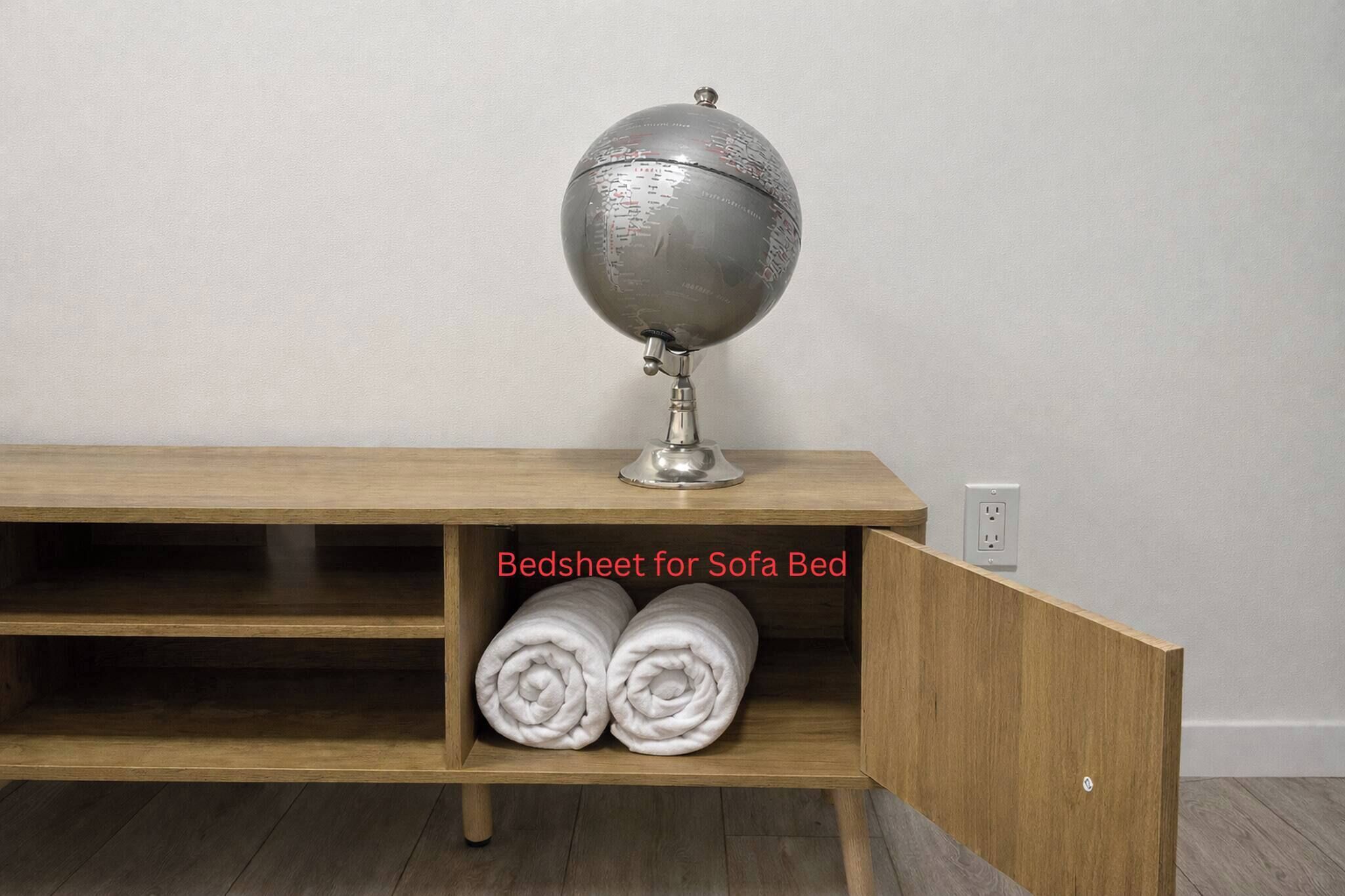 A wooden console bed with a globe lamp on top and a shelf below holding two rolled white towels.