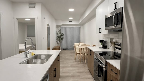 A modern kitchen with a central island, stainless steel appliances, and a dining area with wooden chairs. - Condo w 2 Beds 13 Mins From West Edmonton Mall (Edmonton)