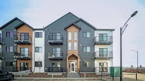 A multi-story residential building with a central entrance, balconies, and a parking area in front. - Condo w 2 Beds 13 Mins From West Edmonton Mall (Edmonton)