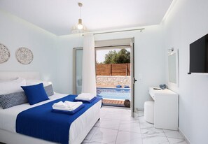A modern bedroom with a bed, a small bathroom, and a view of an outdoor swimming pool. - Primavera Villas - 2 Heated Pools Jacuzzis (Rethymno)