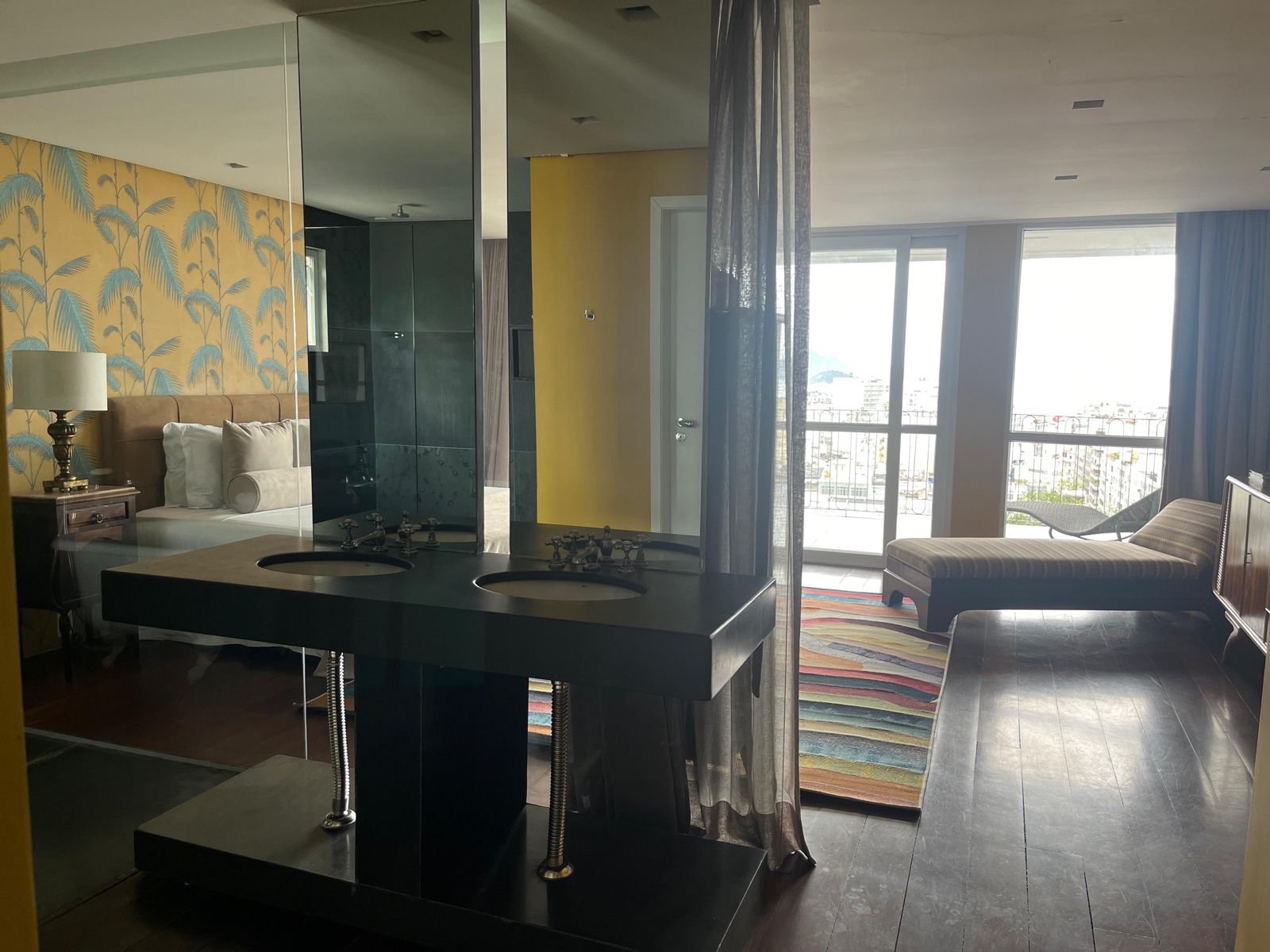 Habitación de hotel moderna con un espejo grande, dos lavamanos, un sofá y vistas a la ciudad.