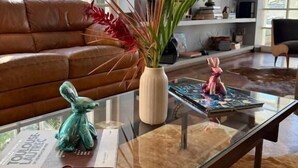 Un soggiorno moderno con un divano in pelle, un tavolino in vetro e una libreria piena di oggetti decorativi.