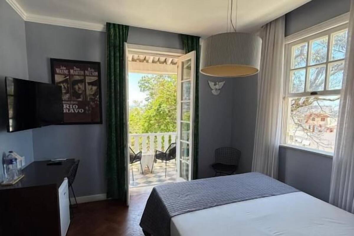 A hotel room with a bed, a desk with a chair, a television, and a balcony with chairs.
