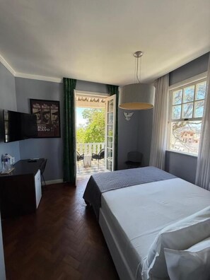 Ein Hotelzimmer mit einem Bett, einem Schreibtisch mit Stuhl, einem Fernseher und einem Balkon mit Sitzgelegenheiten.