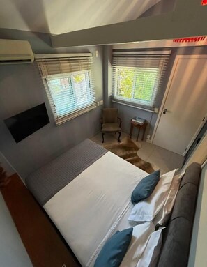 Una camera da letto con un letto, due finestre con tende, una sedia, un tavolino e una porta.