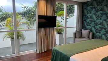 Una habitación de hotel con un ventanal grande, una cama, un televisor y vistas a zonas verdes.