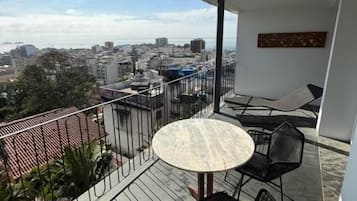 A balcony with a round table and chairs, overlooking a cityscape.