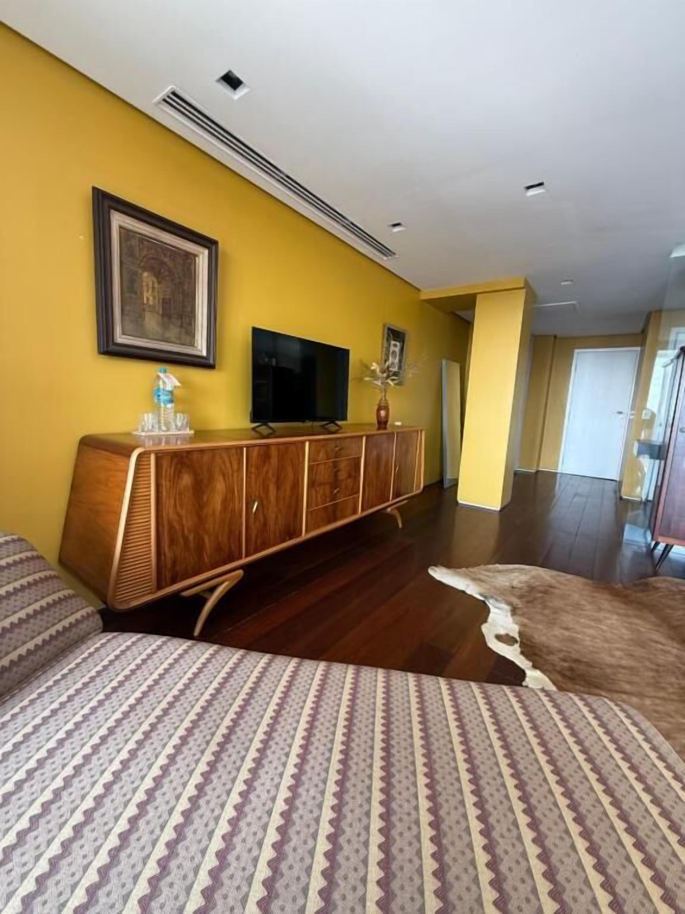 A hotel room with a wooden cabinet, a flat-screen TV, a patterned rug, and a large mirror.