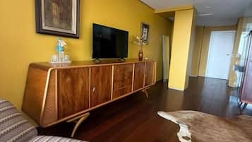 A hotel room with a wooden cabinet, a flat-screen TV, a patterned rug, and a large mirror.