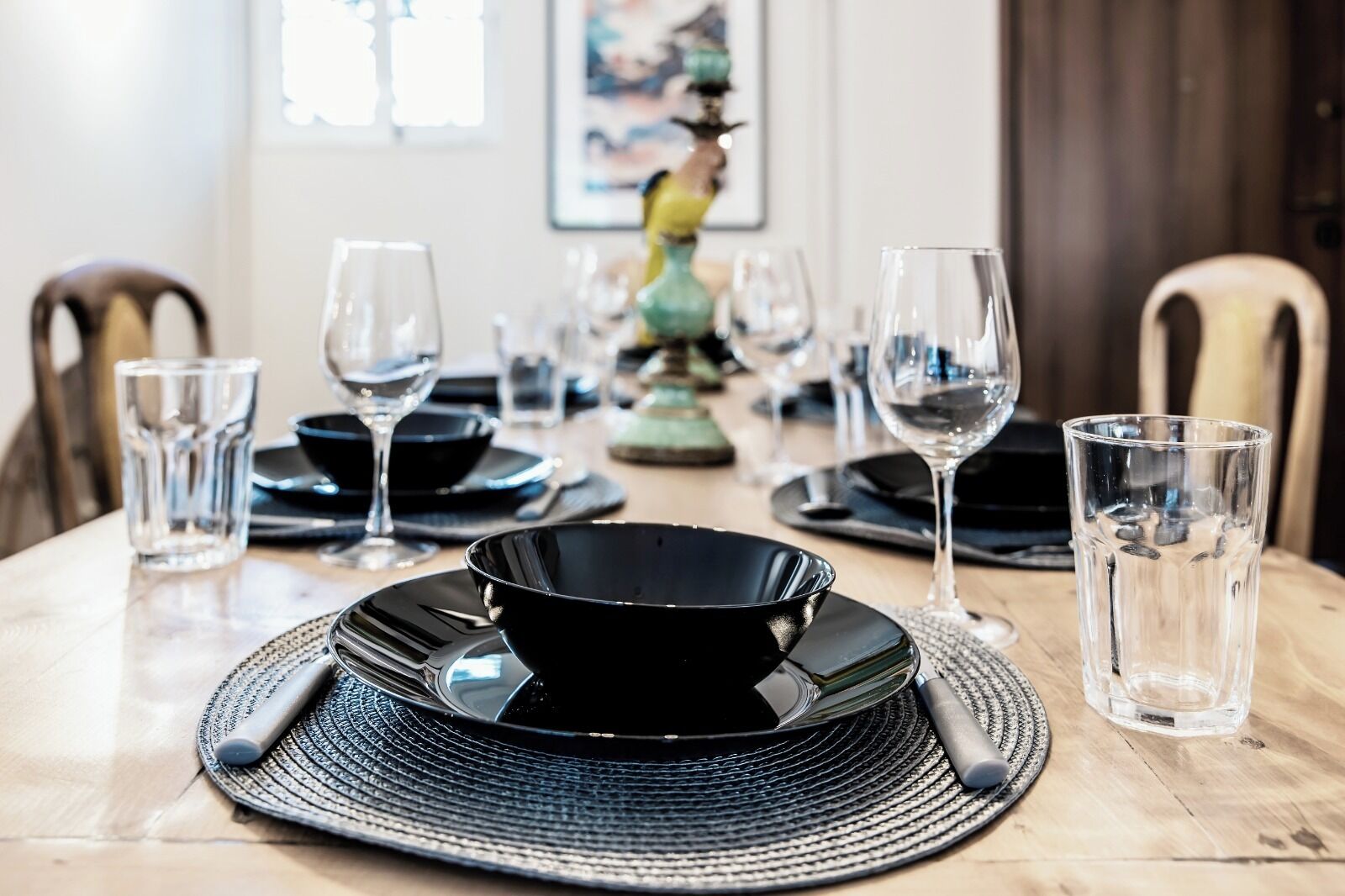 Een eettafel gedekt met zwarte borden, glazen en een geweven placemat.