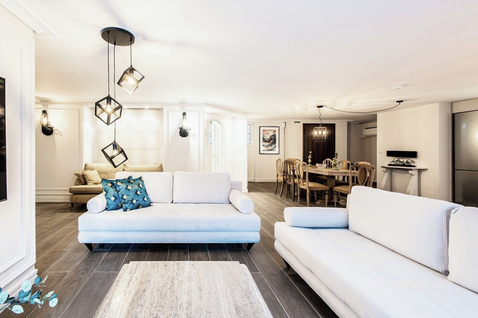 Ein modernes Wohnzimmer mit einem weißen Sofa, einem Essbereich mit einem Holztisch und einer Küche mit einem Edelstahlkühlschrank.