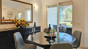 Un coin repas comprenant une table ronde, quatre chaises, un buffet noir, un miroir et un vase rempli de fleurs jaunes.