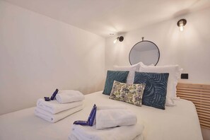 Una habitación de hotel con una cama bien hecha, toallas blancas y un espejo redondo en la pared.