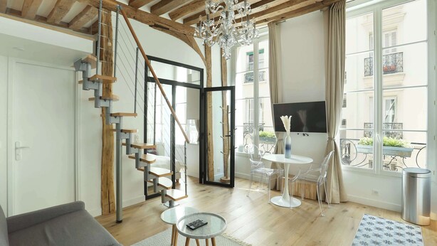 Een moderne woonkamer met een trap, een kroonluchter en uitzicht op het buitenbalkon.