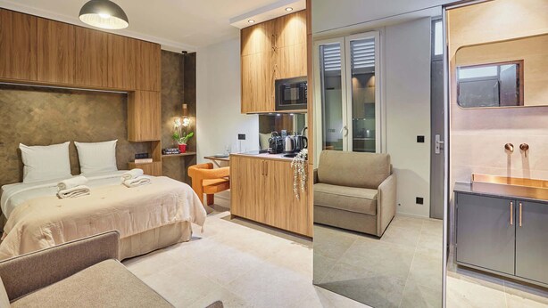 Quarto de hotel moderno com cama, uma pequena mesa de trabalho, cozinha compacta e área de estar.