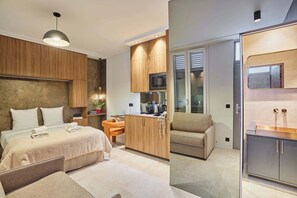 Moderni hotellihuone, jossa on sänky, pieni työpöytä, minikeittiö ja oleskelualue.