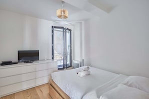 Un dormitorio moderno con cama, televisor sobre un tocador blanco y balcón con vistas.