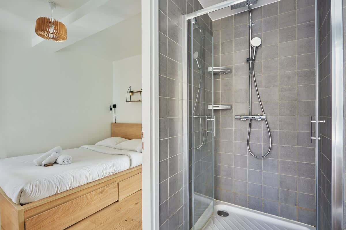 A modern bedroom with a wooden bed, a glass shower enclosure, and a hanging light fixture.