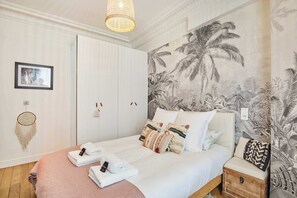 A bedroom with a bed, a nightstand, a wall-mounted shelf, and a tropical-themed wallpaper. - Superb apartment Invalides Eiffel Tower (Paris)