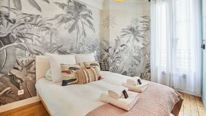 A bedroom with a large bed, tropical wallpaper, and a hanging light fixture. - Superb apartment Invalides Eiffel Tower (Paris)