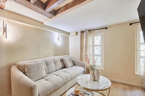 A cozy living room with a beige sofa, a round coffee table, and a window with curtains. - Charming renovated apartment in Center of Paris (Paris)