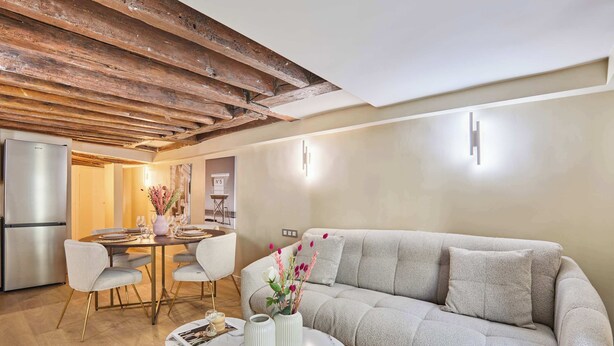 A modern living room with a sofa, dining table, and chairs. There is a kitchen area with a refrigerator and a wooden ceiling. - Charming renovated apartment in Center of Paris (Paris)