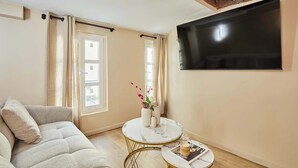 A living room with a sofa, a round coffee table, a flat-screen TV mounted on the wall, and a window with curtains. - Charming renovated apartment in Center of Paris (Paris)