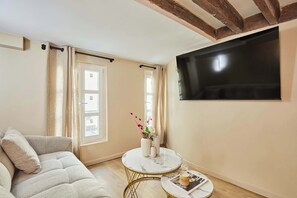 A living room with a sofa, a round coffee table, a flat-screen TV mounted on the wall, and a window with curtains. - Charming renovated apartment in Center of Paris (Paris)