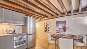 A modern kitchen with stainless steel appliances, a wooden ceiling, and a dining area with a round table and chairs. - Charming renovated apartment in Center of Paris (Paris)