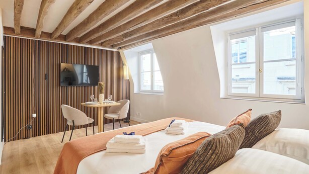 Ett hotellrum med ett träpanelat tak, en säng med kuddar och handdukar, en tv på väggen och ett fönster med utsikt.