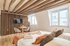 Hotellihuone, jossa on puinen katto, sänky tyynyineen ja pyyhkeineen, seinälle asennettu televisio ja ikkuna, josta on näkymä.