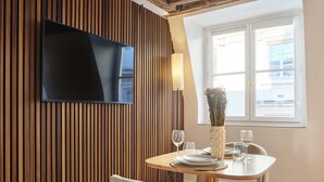En matplats med en väggpanel av trä, en platt-TV som hänger ovanför ett bord dukat med tallrikar, glas och en vas med blommor.