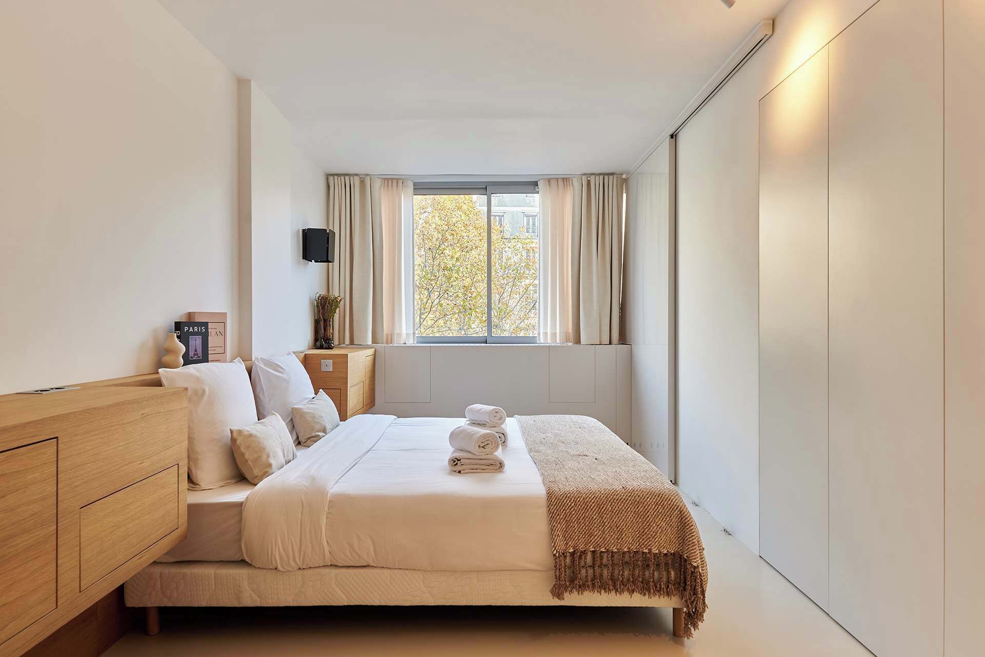 A bedroom with a bed, a bedside table, a TV, and a window with curtains.