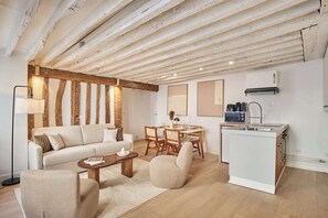 Una sala de estar moderna con sofá, mesa de centro y sillas, un comedor con mesa y sillas, y una cocina compacta con pileta y alacenas.