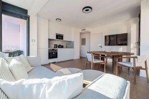 A modern living room with a sofa, a dining table with chairs, a kitchen area with appliances, and a TV mounted on the wall. - Superb terrace apartment in Monaco-Beausoleil (Beausoleil)