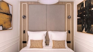 Une chambre d’hôtel avec un grand lit, deux tables de chevet, un luminaire au plafond et des œuvres d’art accrochées aux murs.