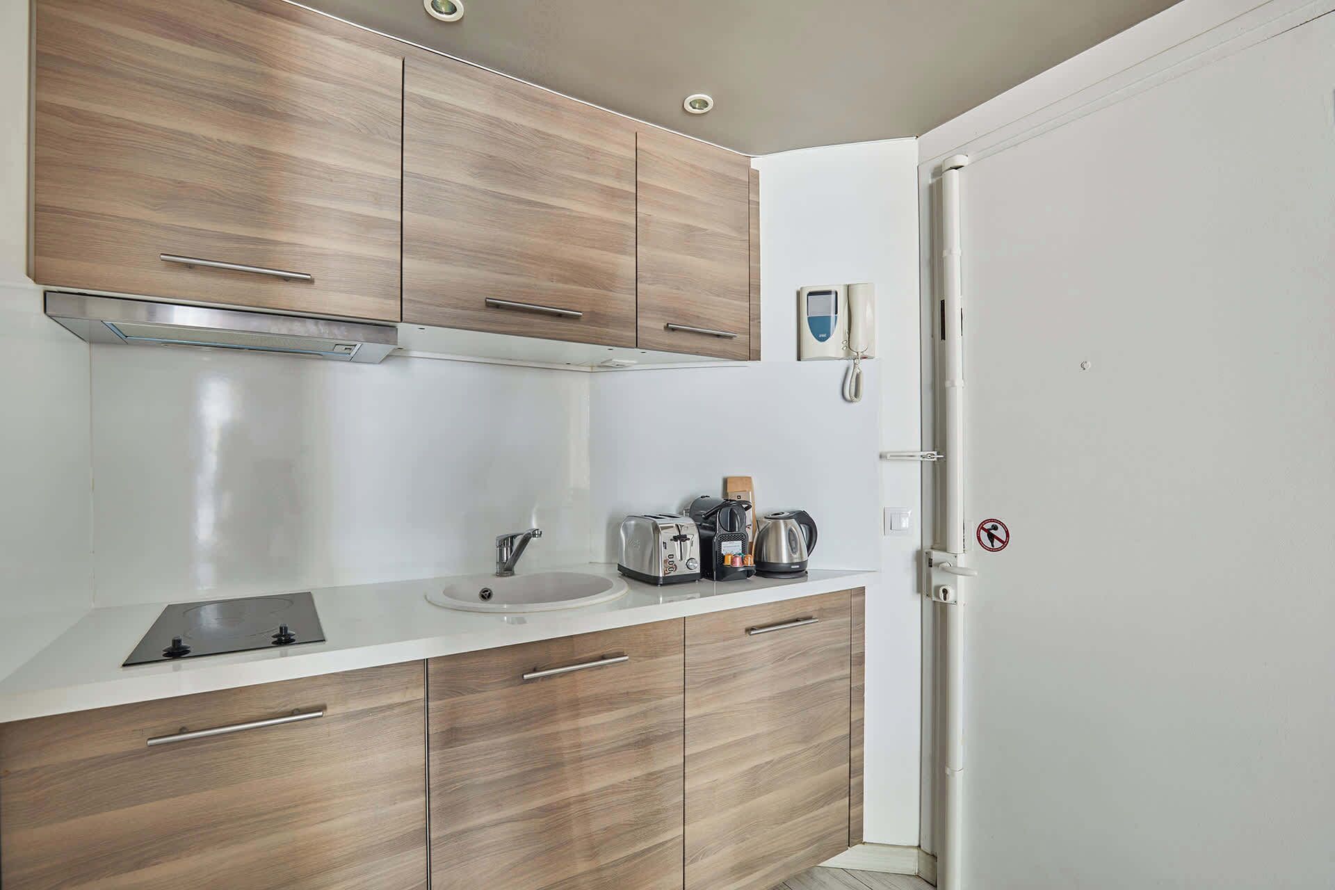 Eine kleine Küche mit Holzschränken, einer weißen Arbeitsplatte, einem Spülbecken und einem Toaster.