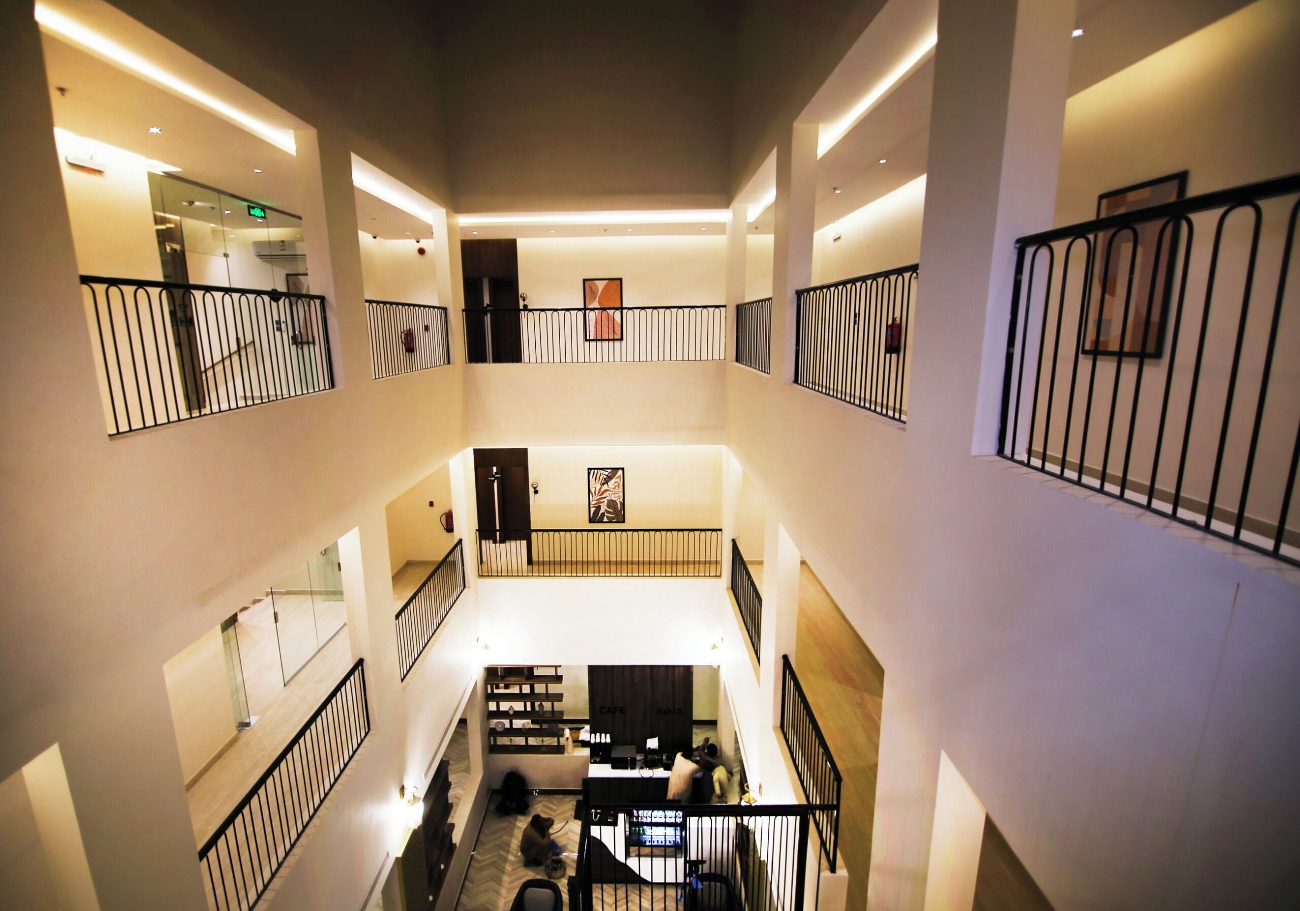 A multi-level hotel interior with a central staircase, railings, and a reception area.