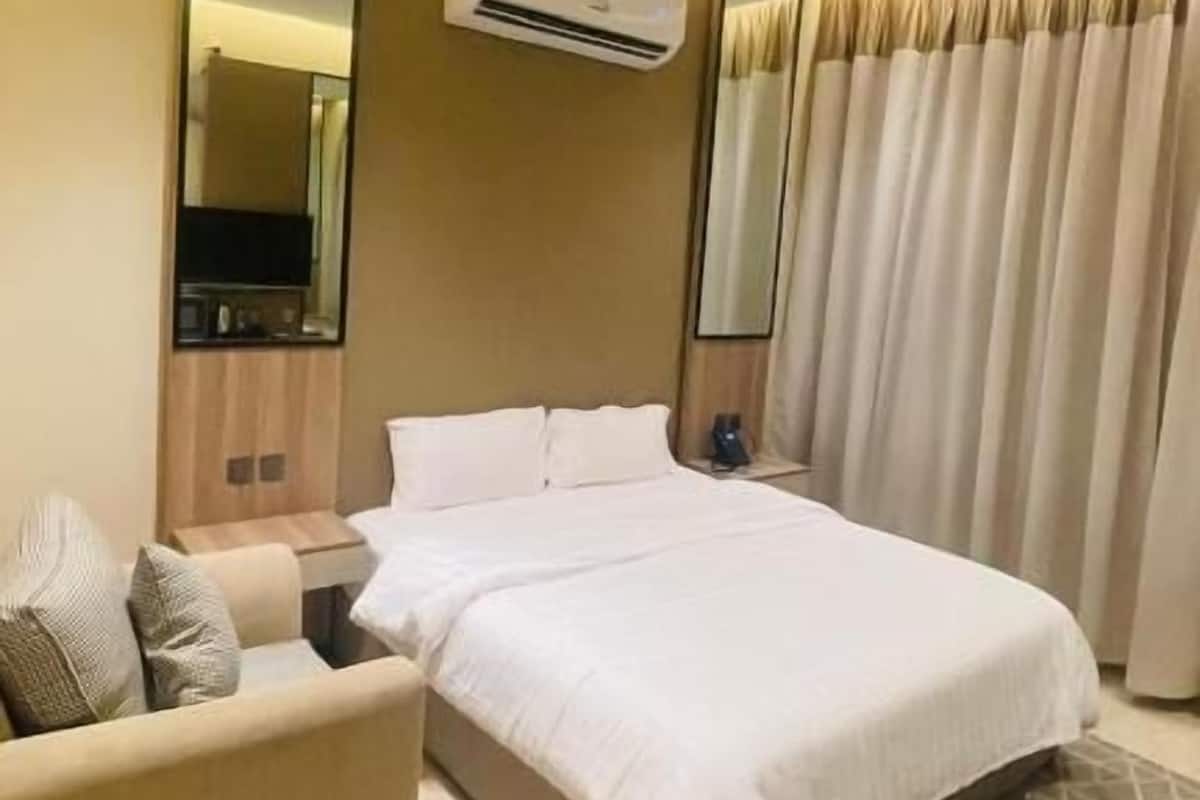 A modern hotel room with a large bed, a sofa, a flat-screen TV, and an air conditioning unit.