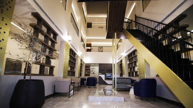 Eine moderne Lobby mit einer zentralen Sitzgruppe, einer Treppe und einem Empfangsschalter.
