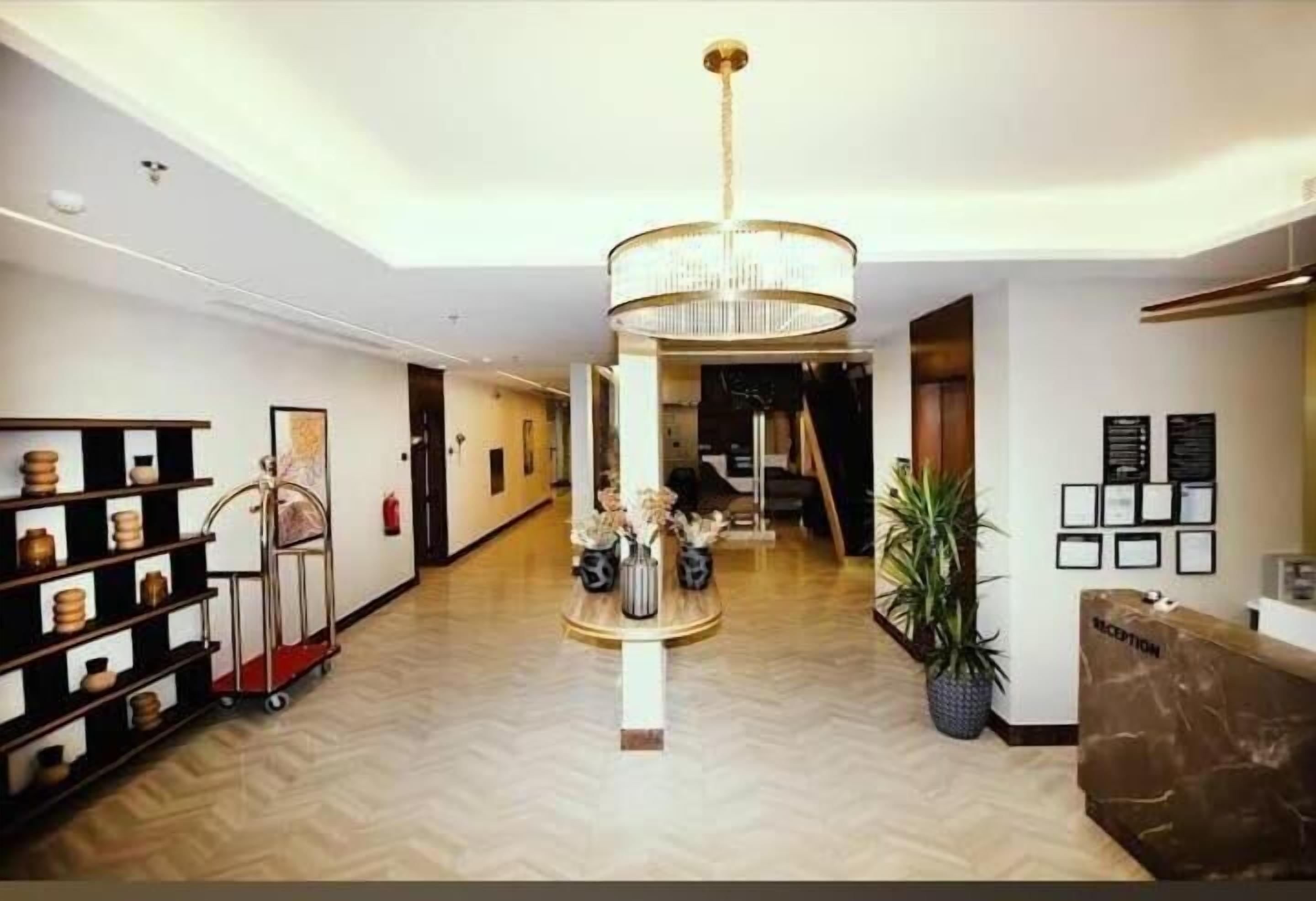 A hotel reception area with a chandelier, reception desk, framed certificates, and a plant.