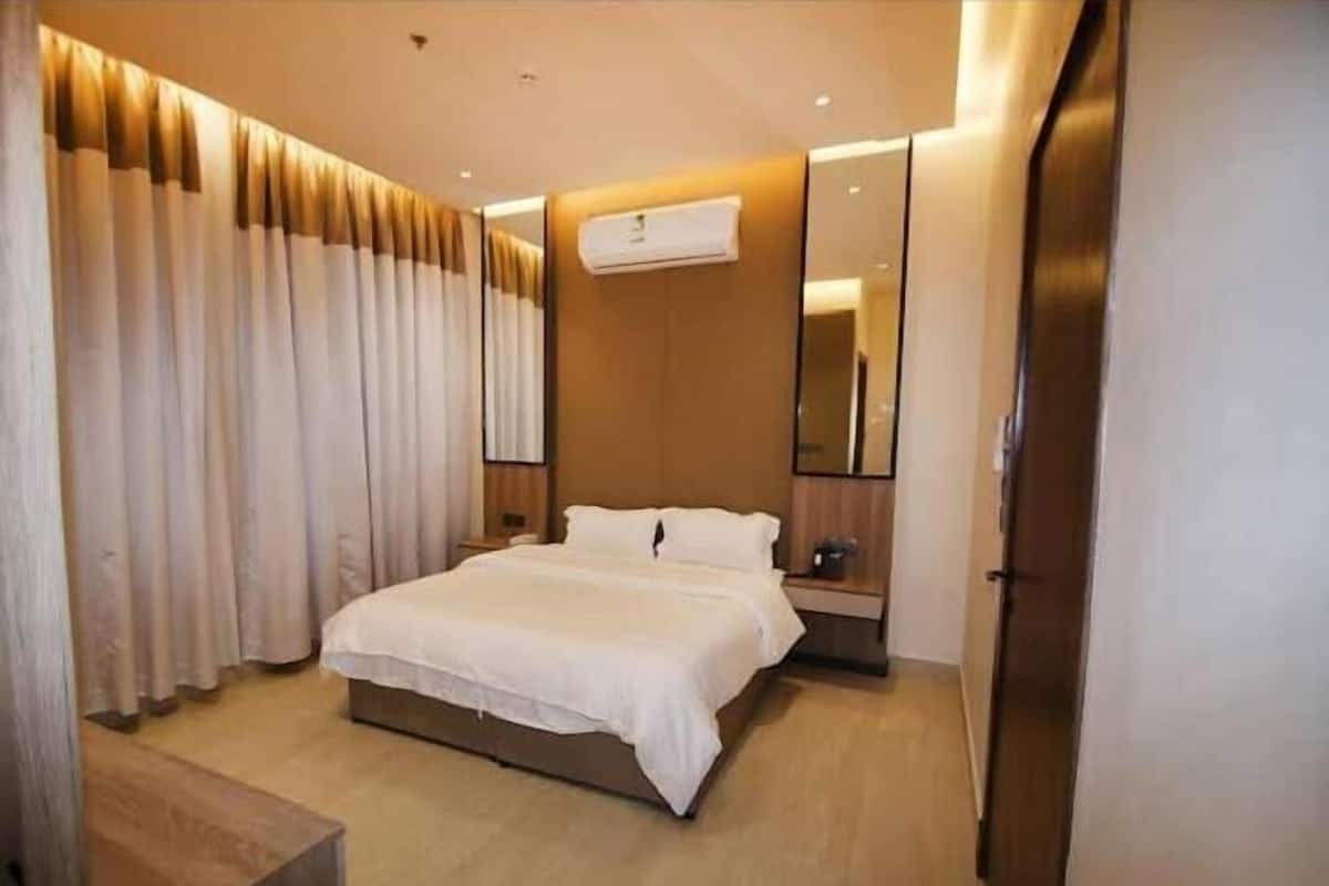 A modern hotel room with a large bed, a bedside table, an air conditioning unit, and a mirror.