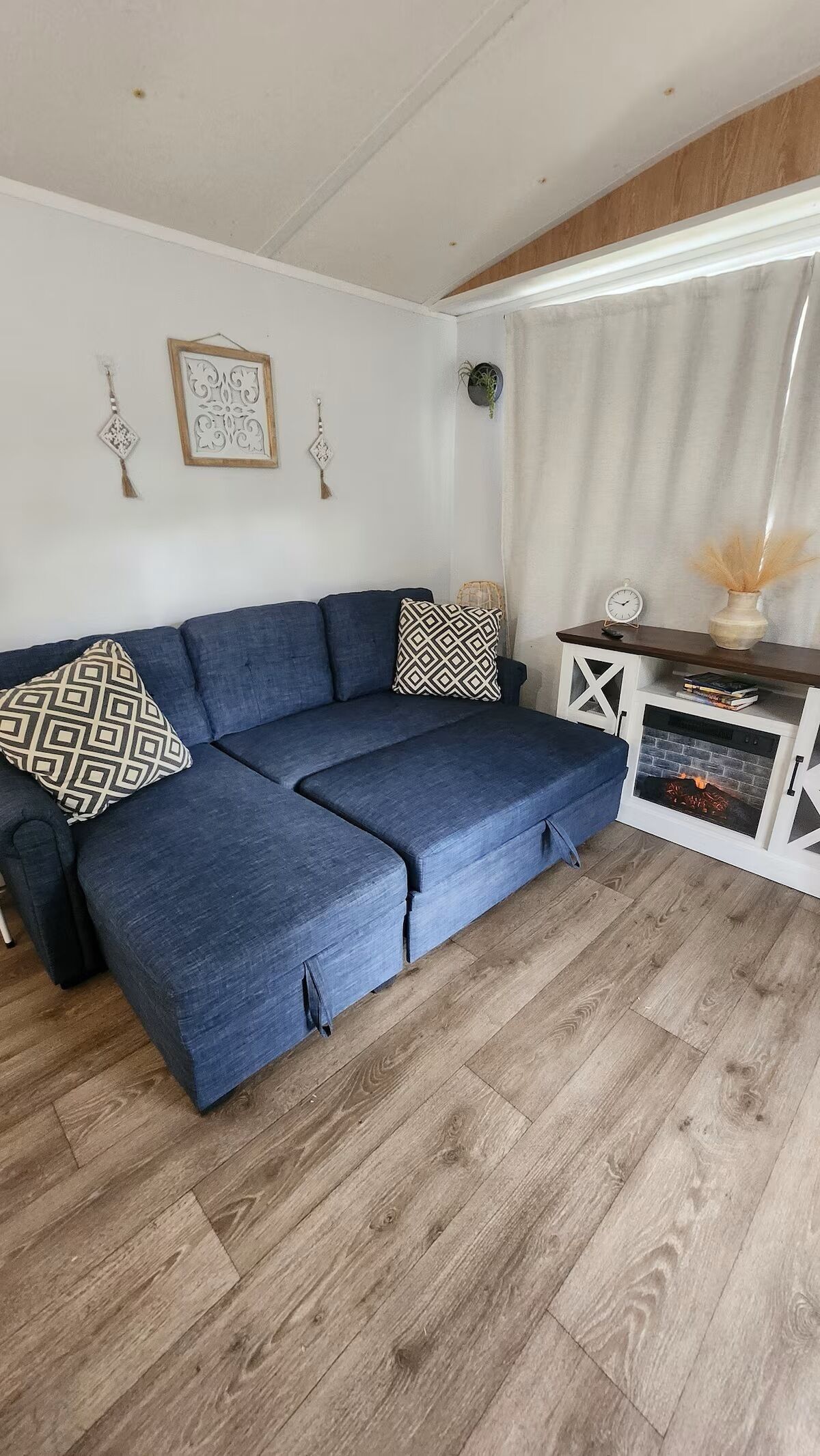 A living room with a blue sofa, patterned cushions, a fireplace, and a white wall with decorative items.