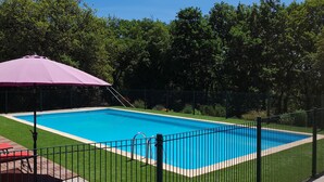 Une piscine rectangulaire entourée d’une clôture, un parasol violet et des chaises longues.
