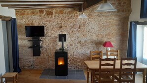 Une pièce chaleureuse avec un mur en pierre, une cheminée, un téléviseur et un coin repas.